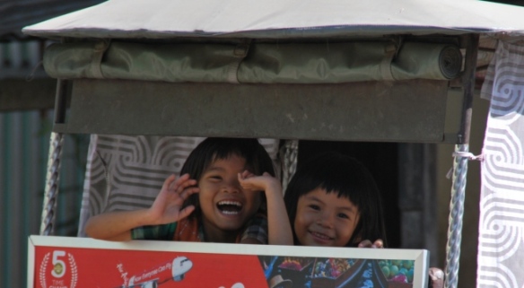 Children wave excitedly from the back of a rickshaw on the streets of Phnom Penh.